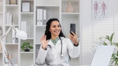 Friendly female doctor video calling on smartphone in clinic