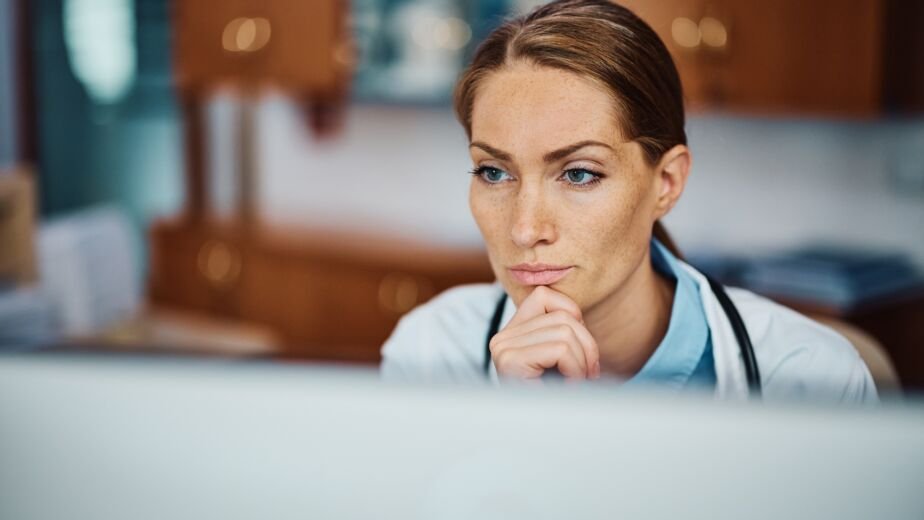 Pensive doctor working on her desktop PC at doctor's office.